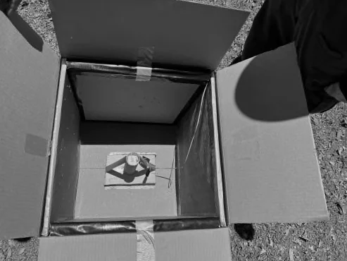 Looking down into a box lined with panels, with a cylindrical charge mounted on foamboard in the center.